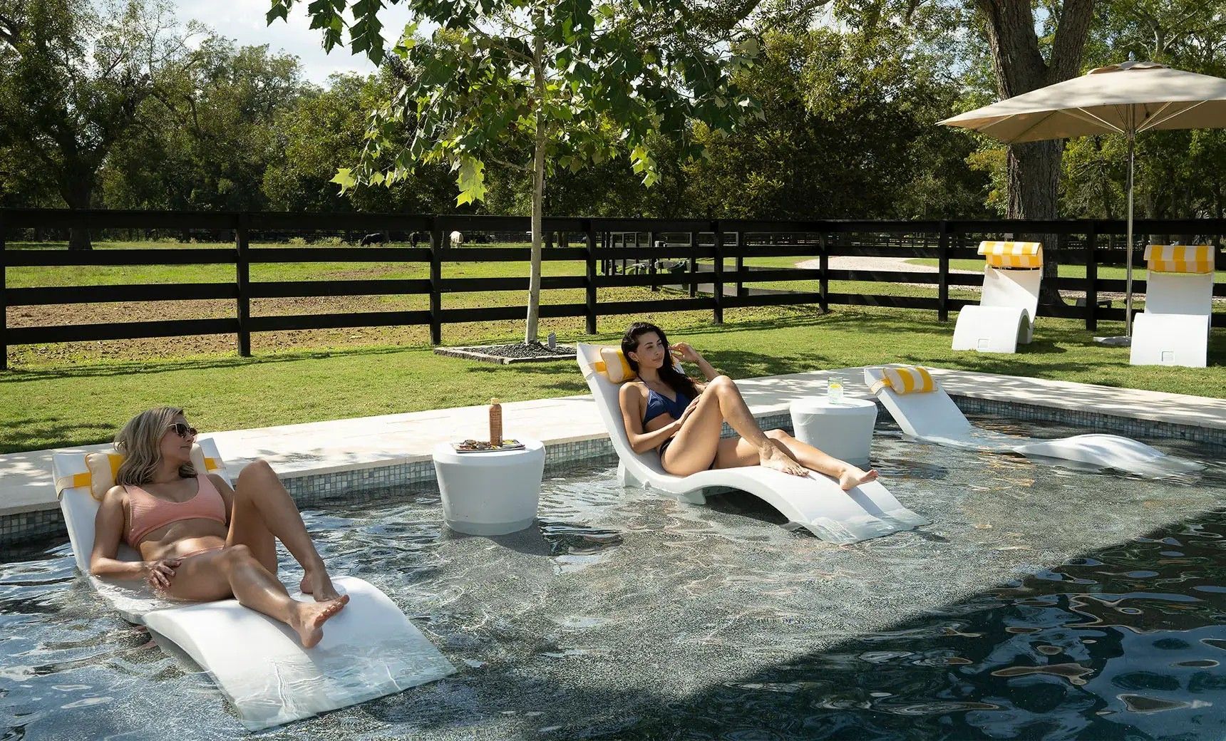 Two women are sitting on lounge chairs in a swimming pool.