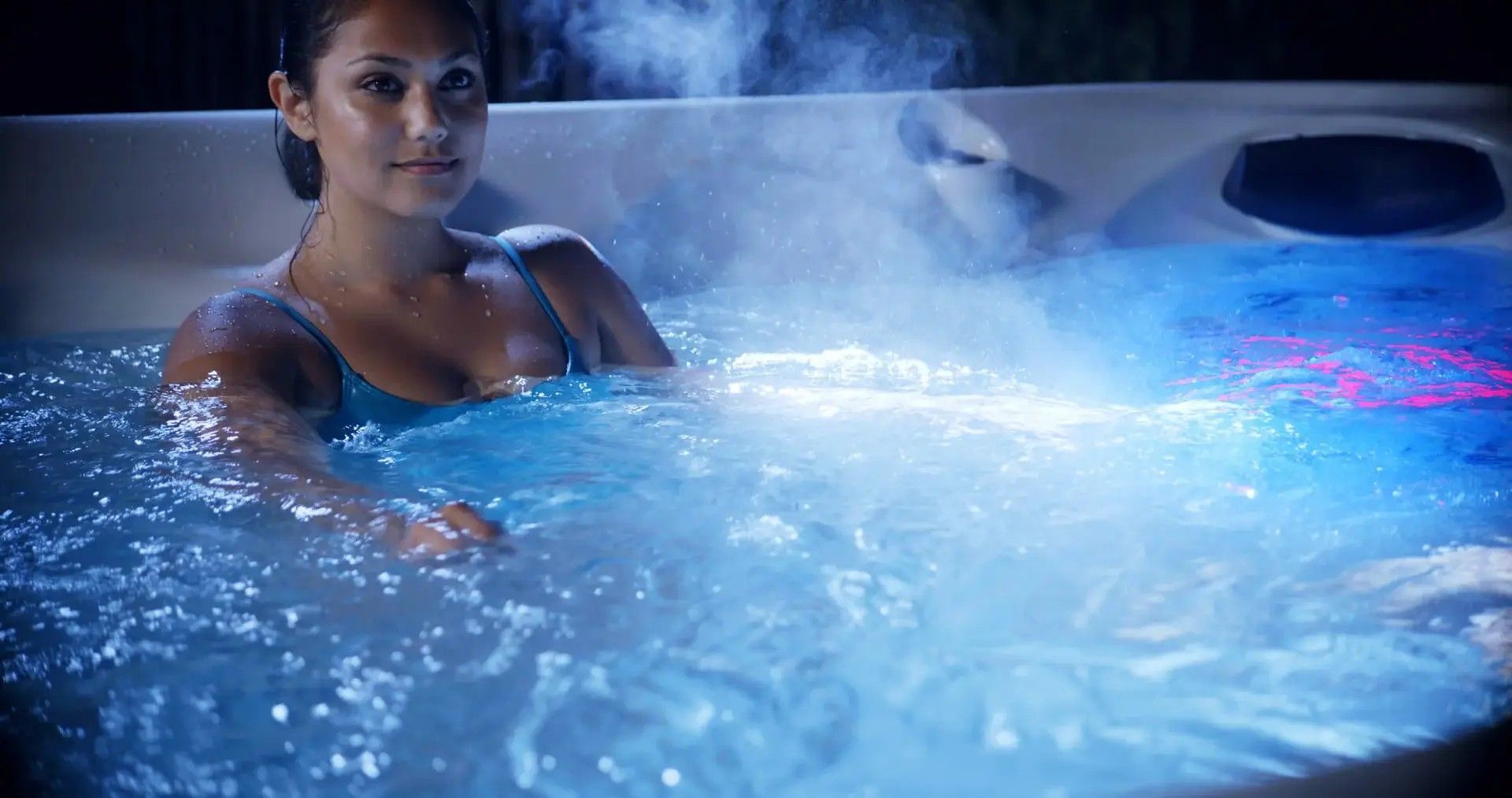 A woman is sitting in a hot tub at night.