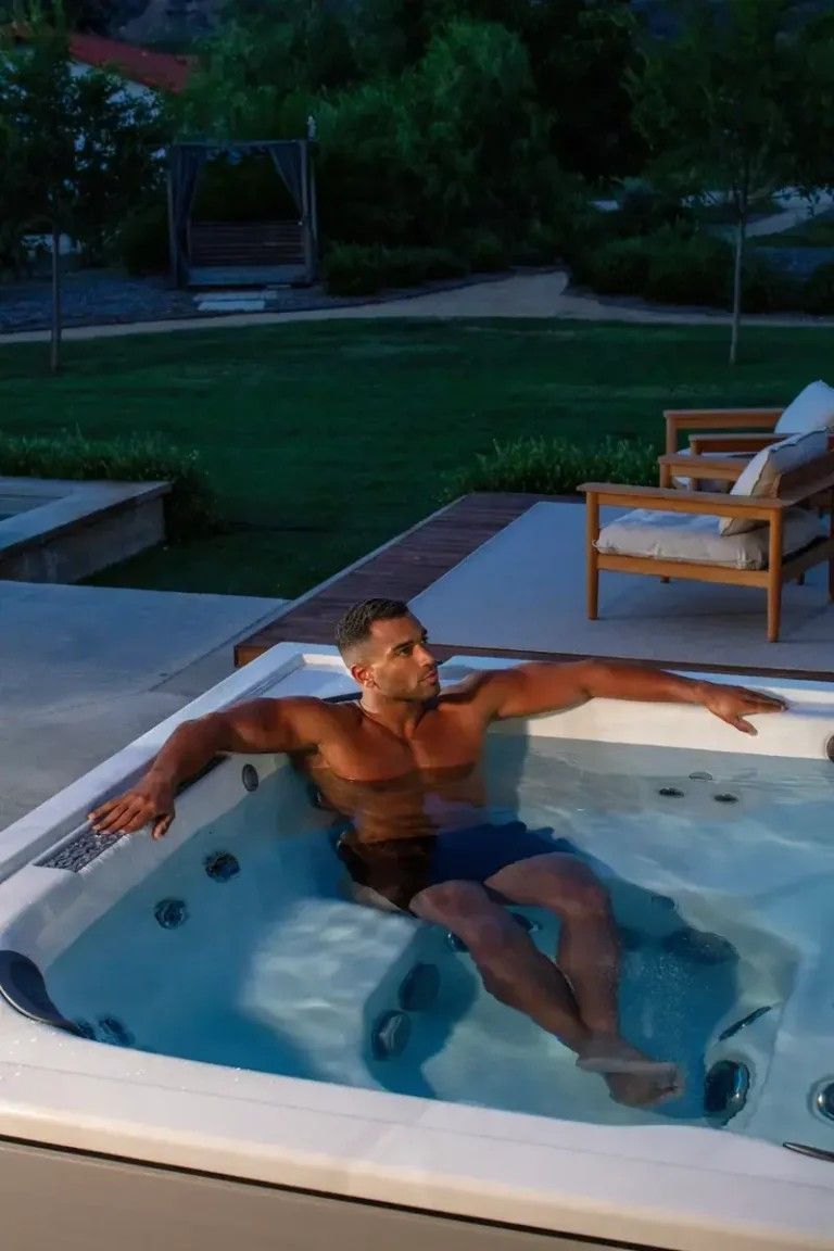 A man is sitting in a hot tub with his arms outstretched.