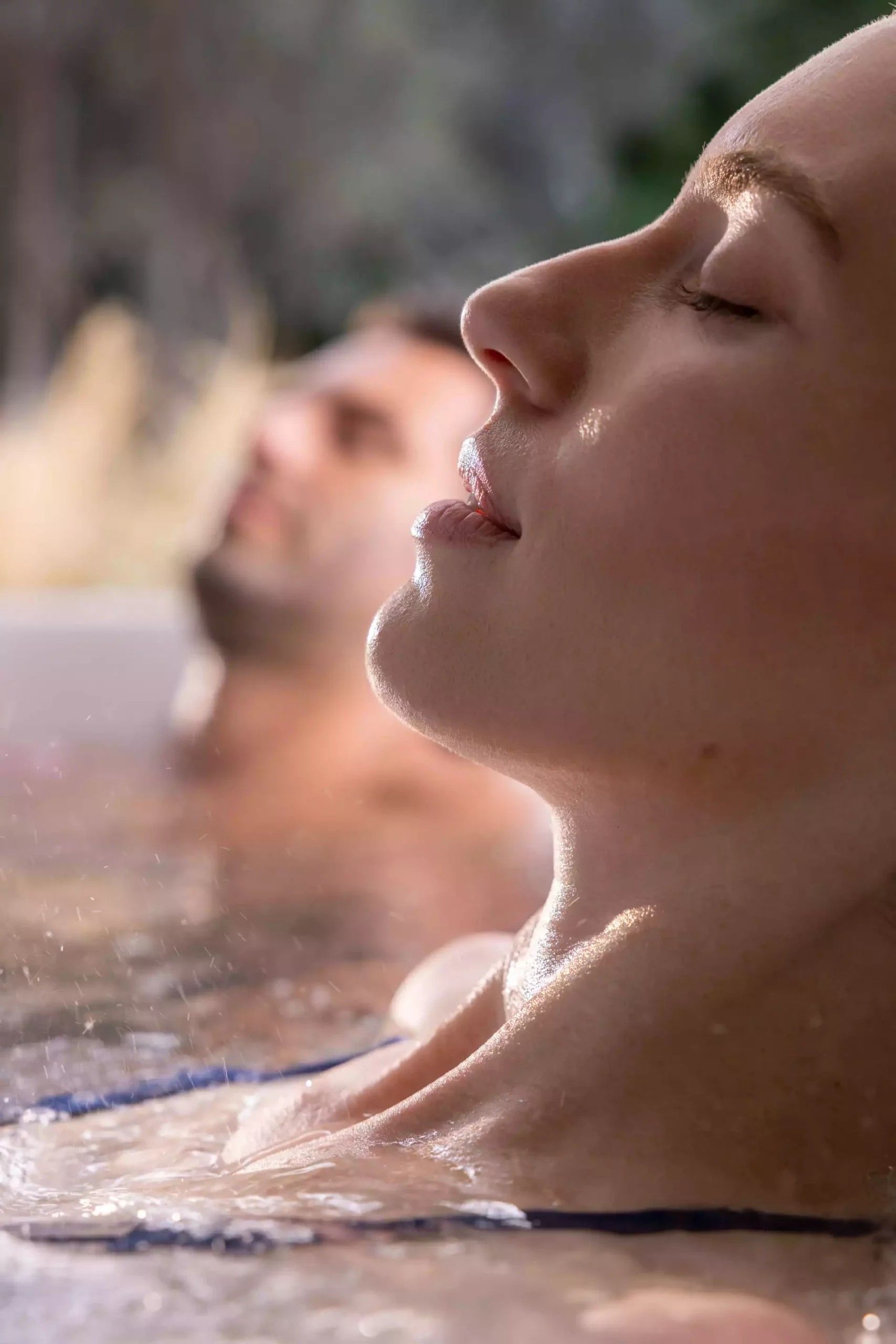 A man and a woman are laying in a hot tub with their eyes closed.