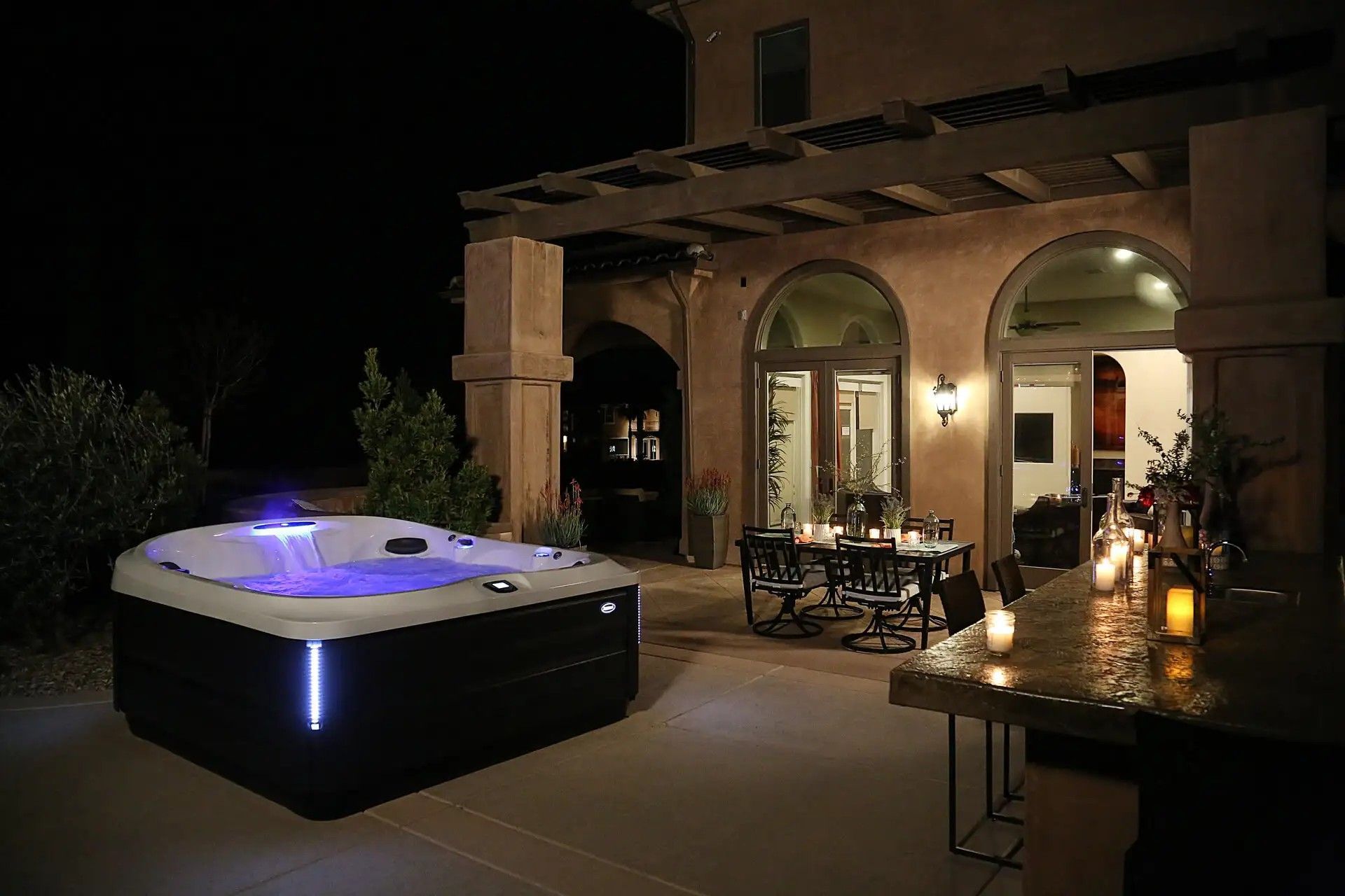 A hot tub is sitting on a patio next to a table and chairs at night.