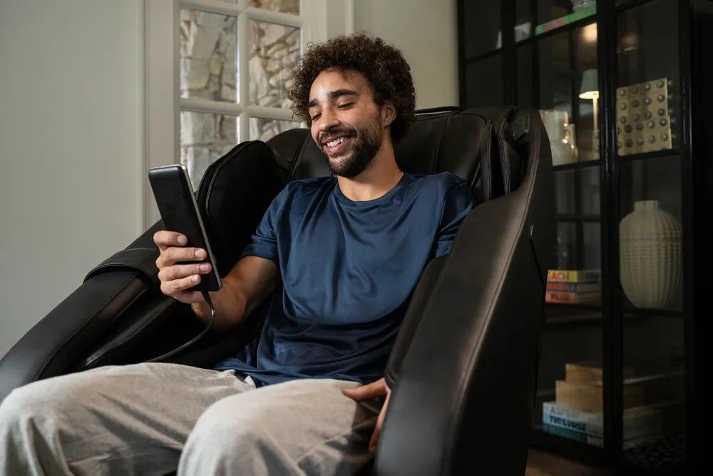 A man is sitting in a massage chair using a tablet.