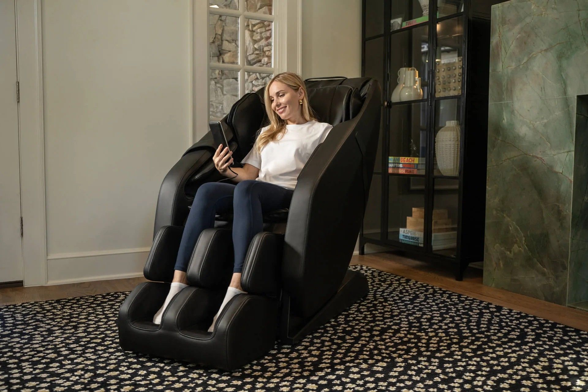 A woman is sitting in a black massage chair in a living room.