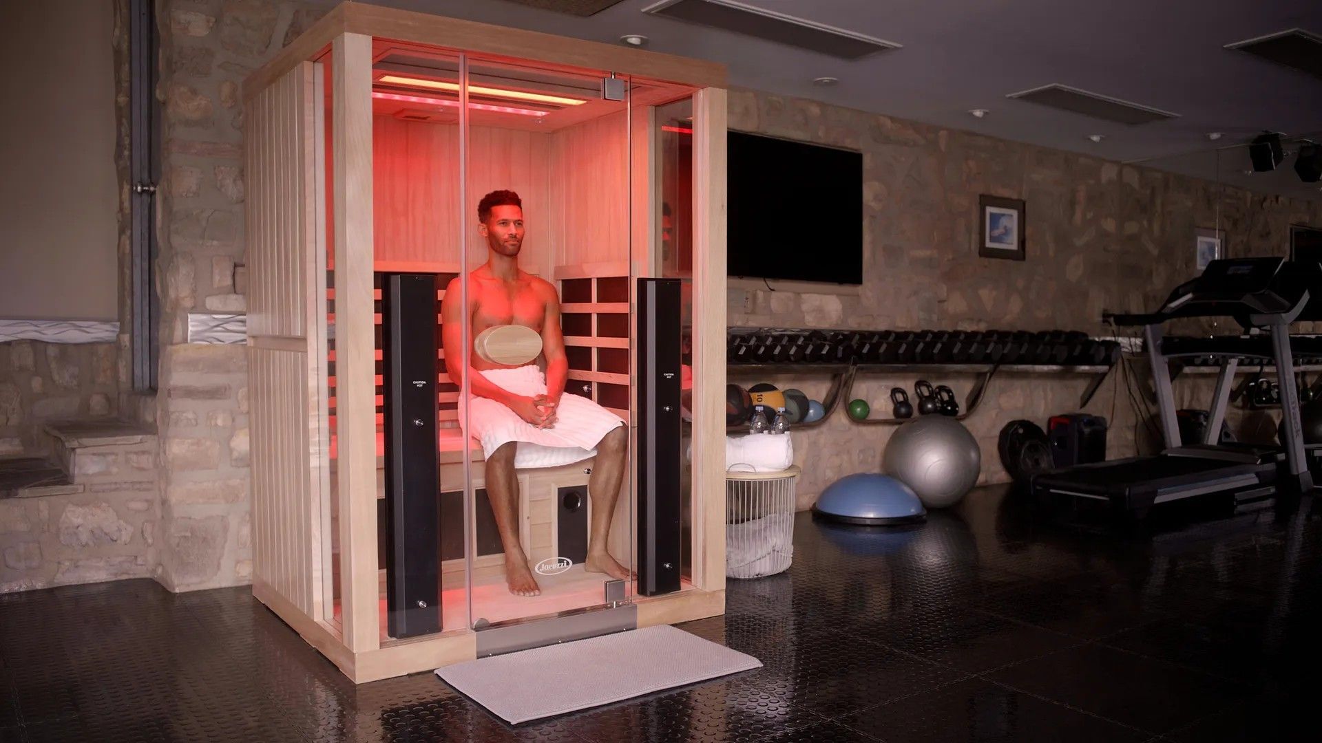 A man is sitting in an infrared sauna in a gym.