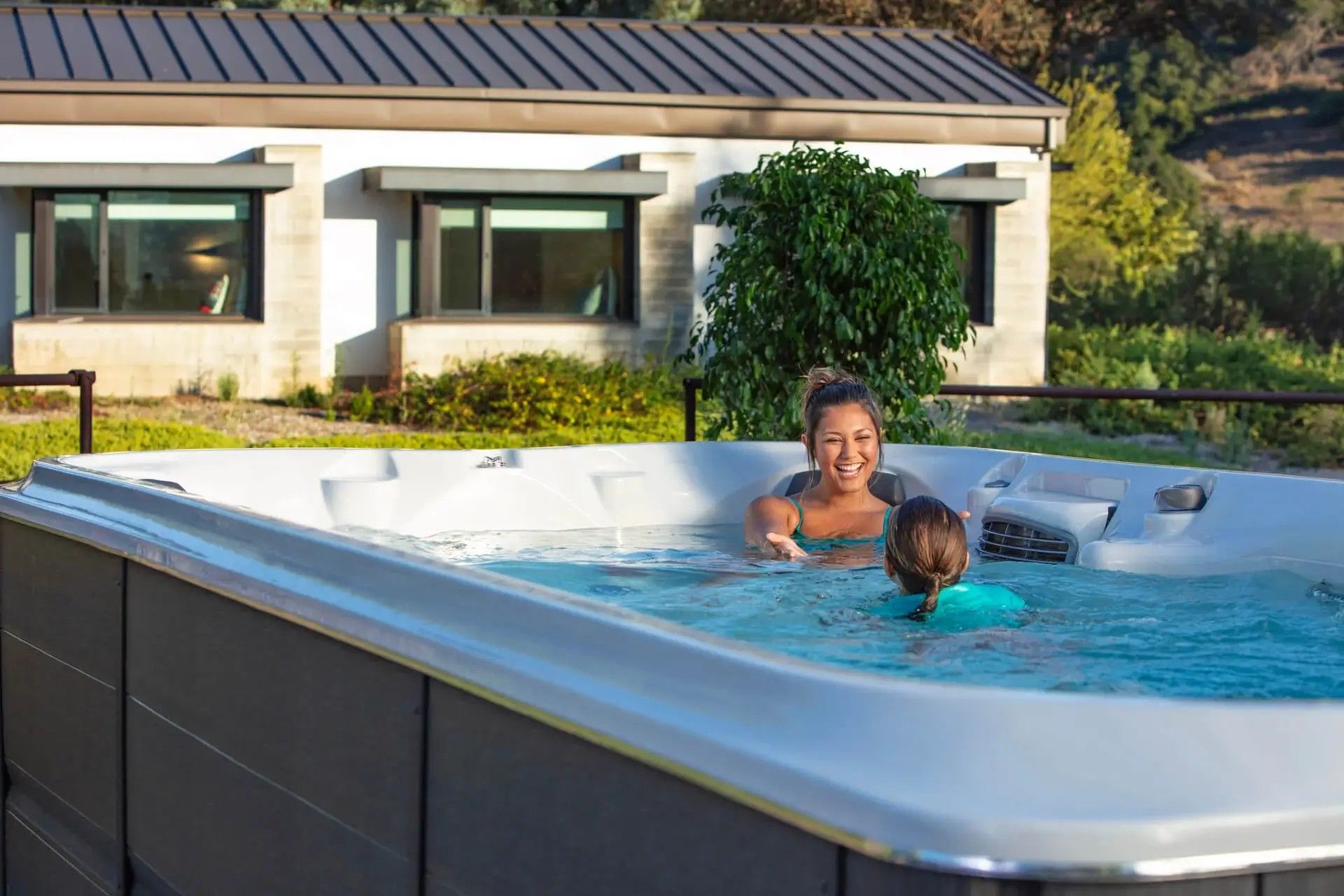 A woman and a child are swimming in a hot tub in front of a house.
