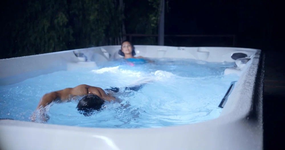 Two people are swimming in a hot tub at night.