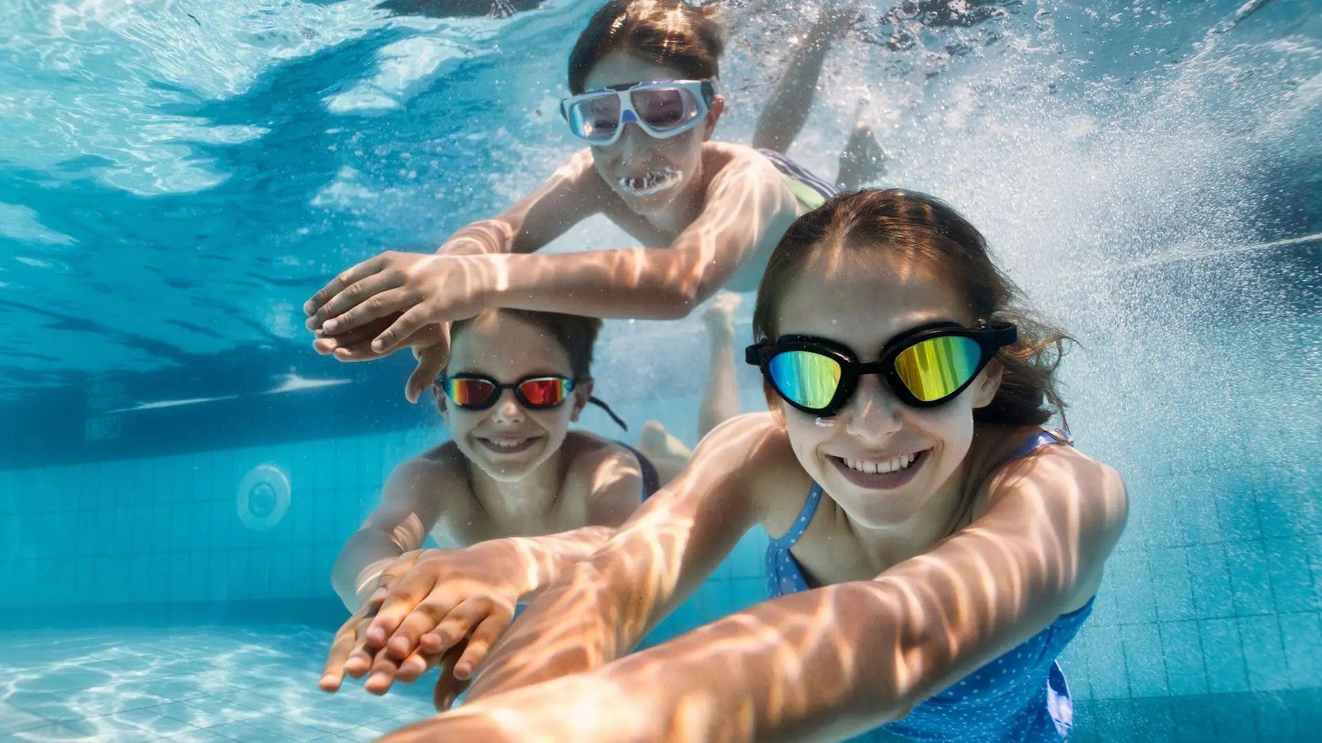 Three children are swimming underwater in a swimming pool.
