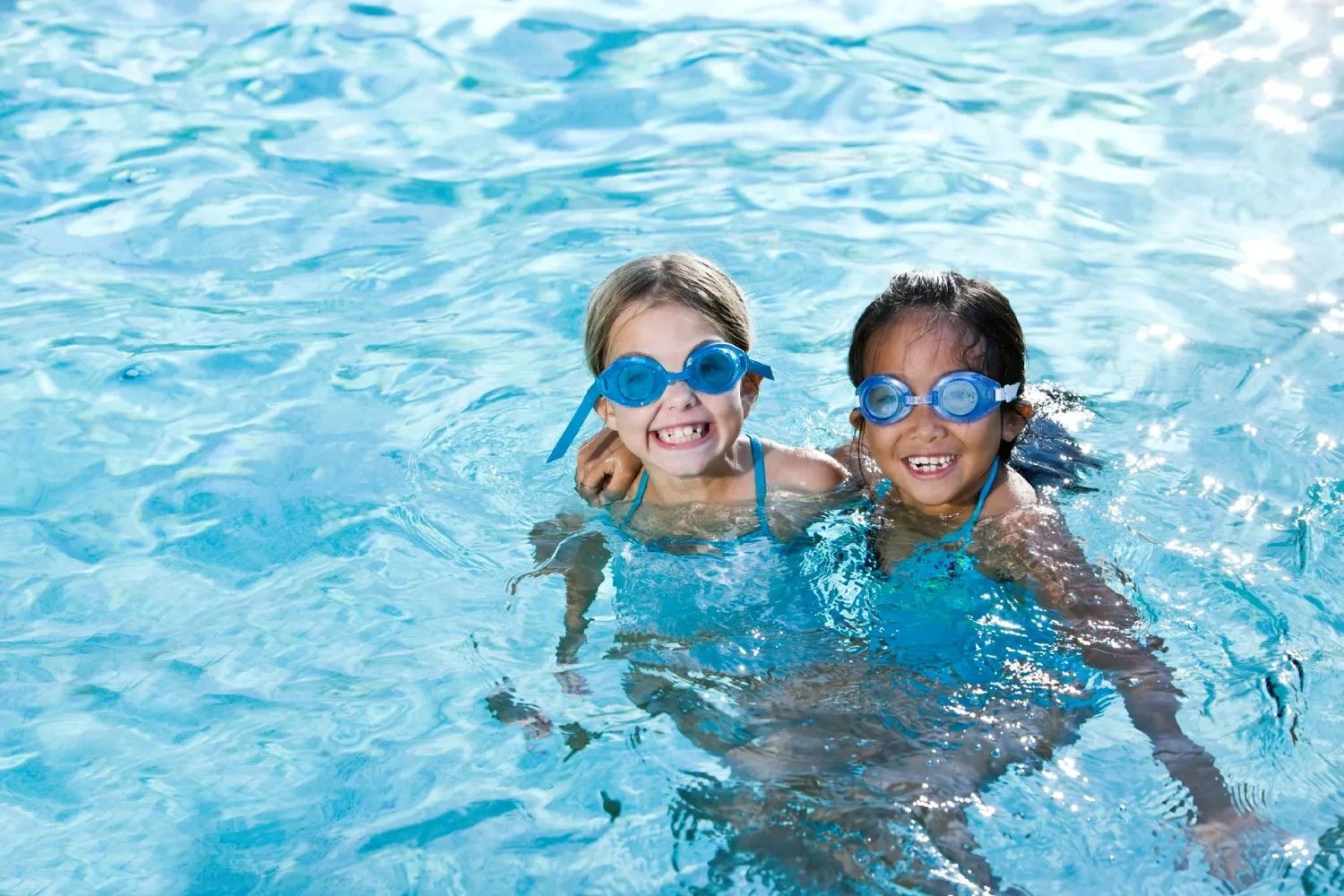 Two young girls wearing goggles are swimming in a pool.