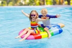 A boy and a girl are sitting on an inflatable ice cream in a swimming pool.