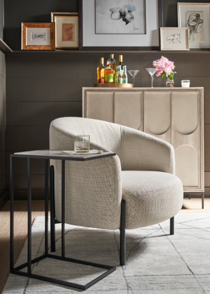 Modern living room with beige curved chair, black side table, and sideboard with bottles and flowers