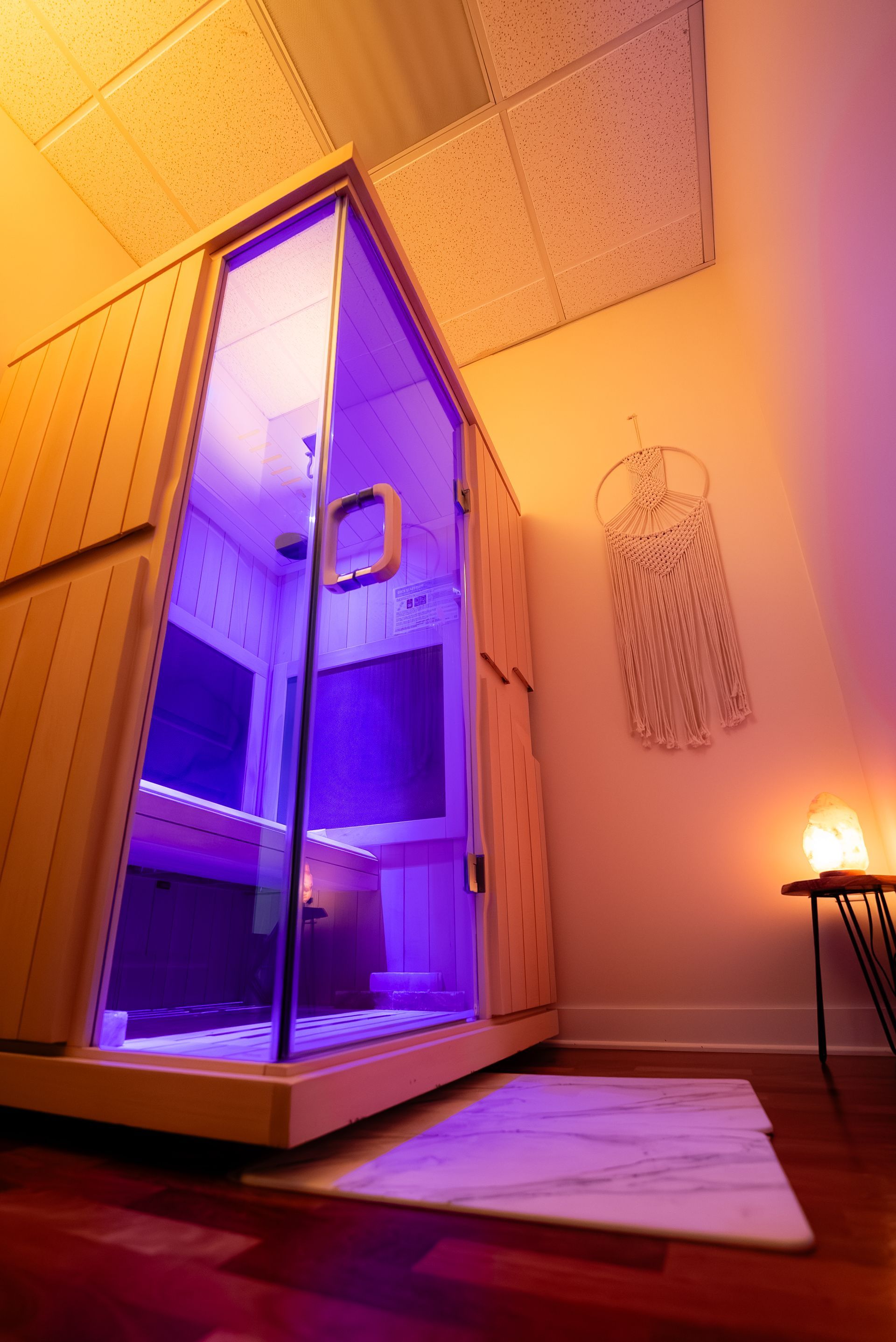 Wooden infrared sauna with purple light, glass door, in a softly lit room with decor