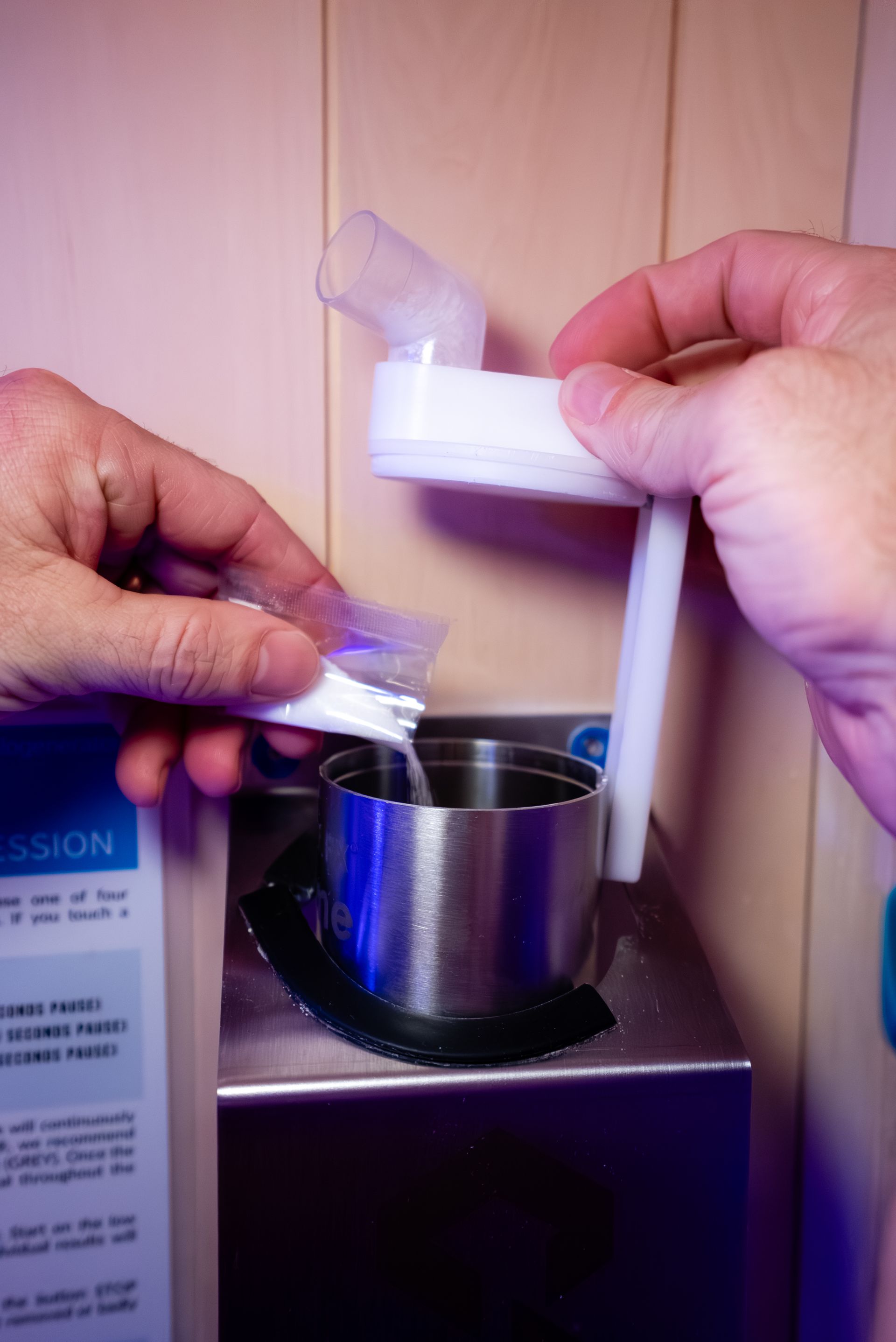 Hands pouring salt from a packet into a metal container in a sauna setting
