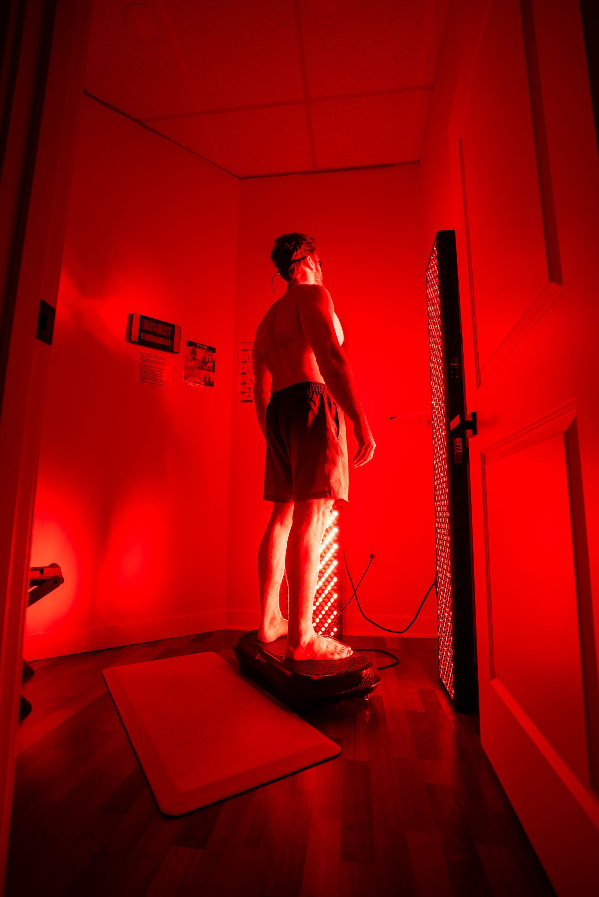 Person standing in a red-lit room facing a vertical panel of lights