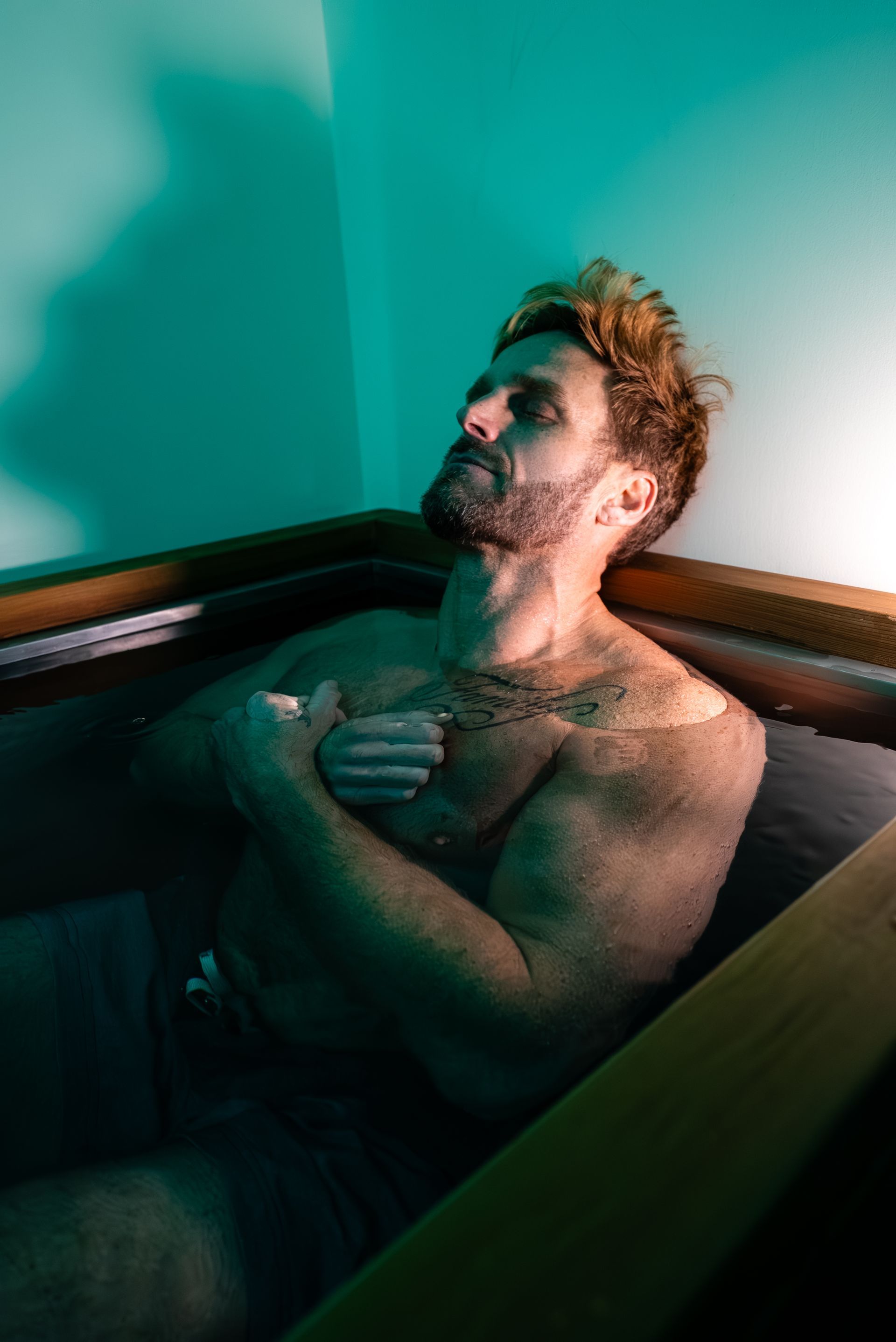 Man relaxing in a cold plunge tub, eyes closed, hand on chest