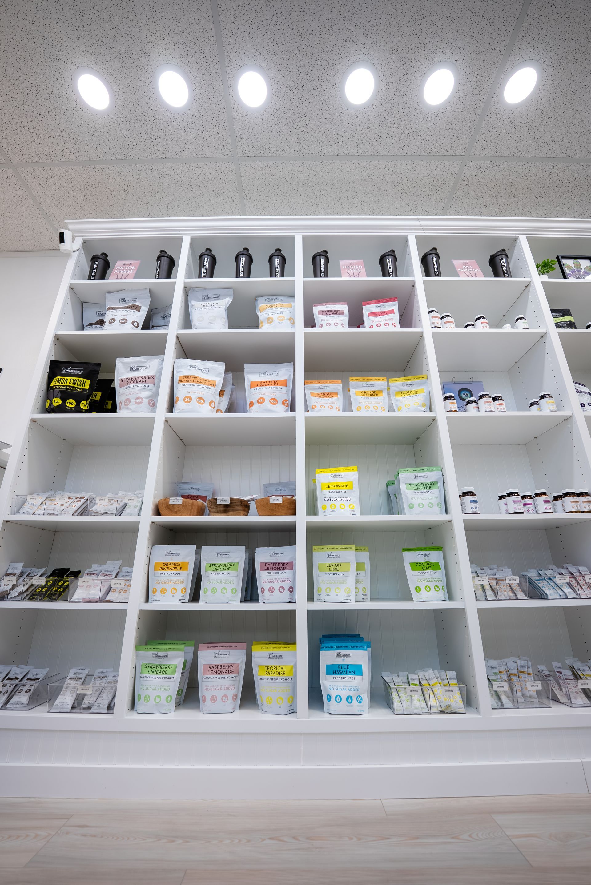 White shelving unit displaying various packaged products, set against a white wall and ceiling with overhead lighting