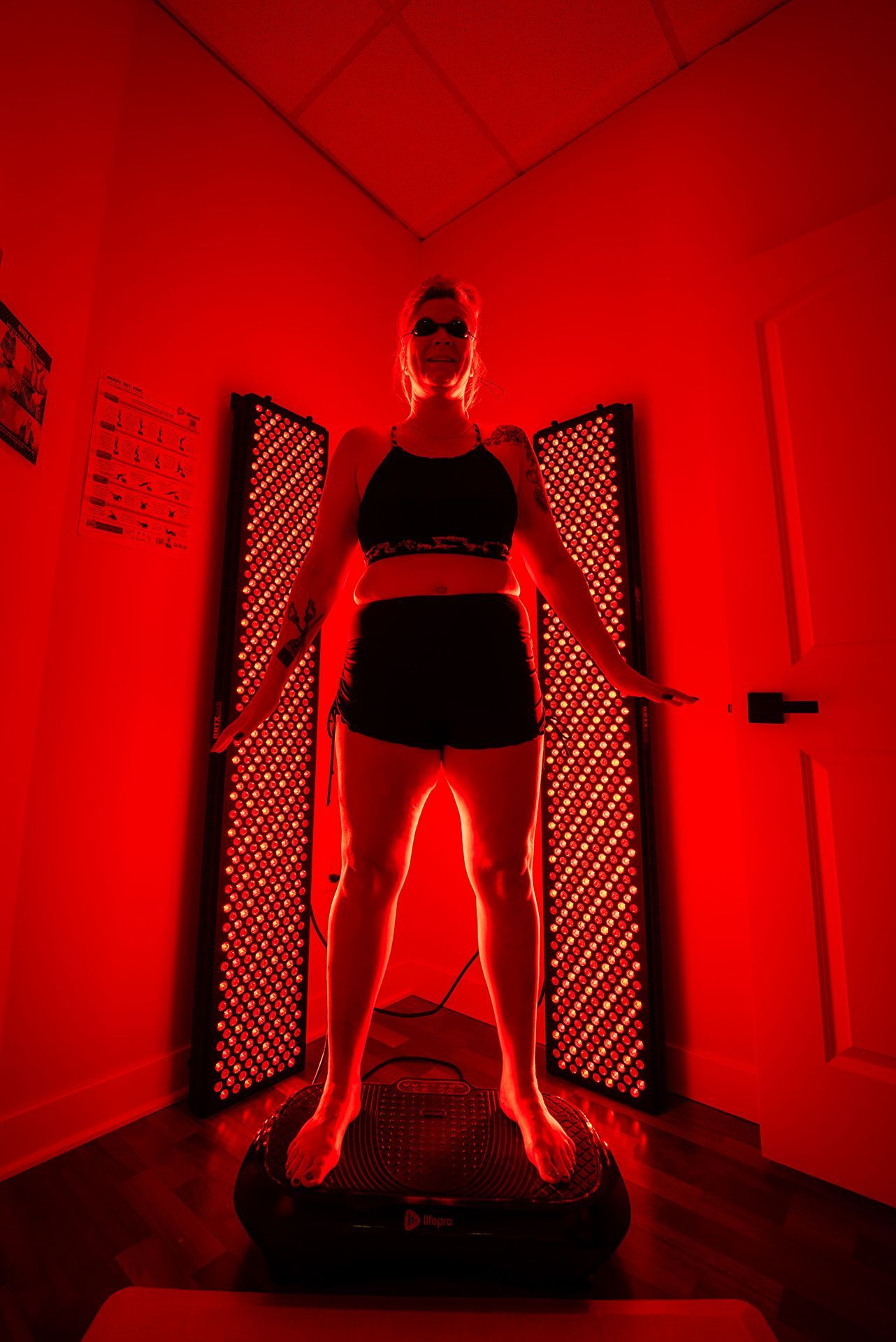 Woman stands in red light therapy booth with arms outstretched