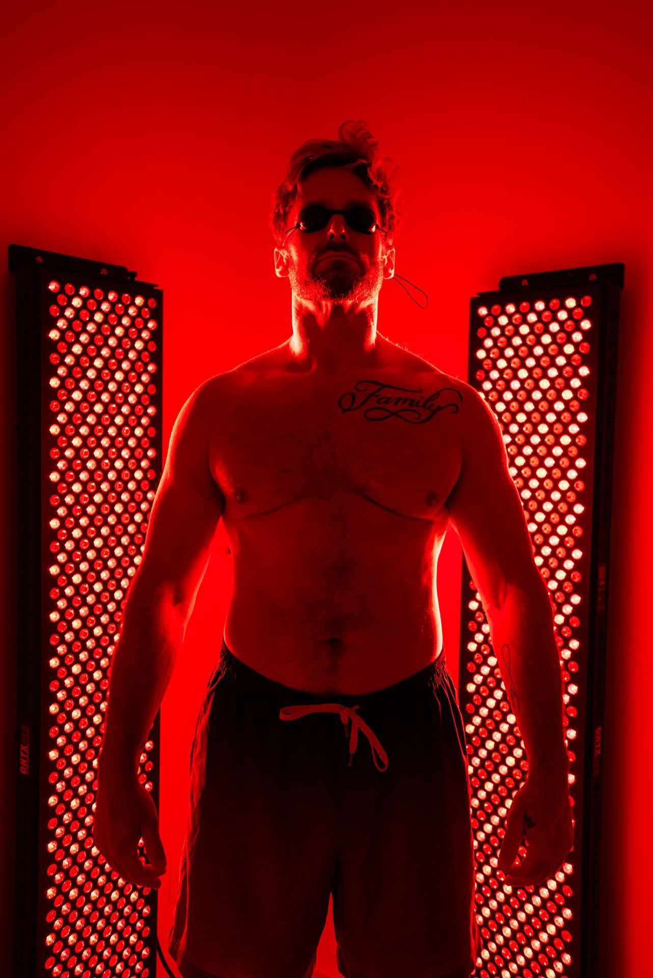 Shirtless man standing between two red light therapy panels