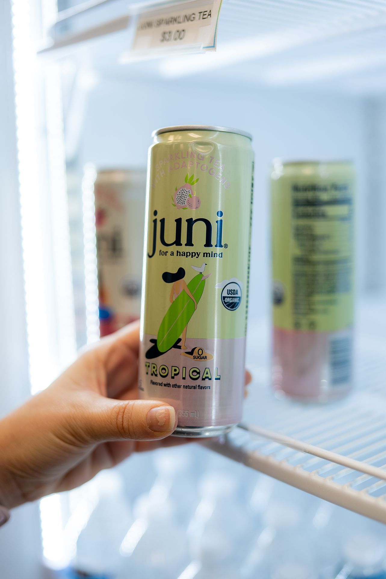 Hand reaching for a Juni drink in a refrigerator