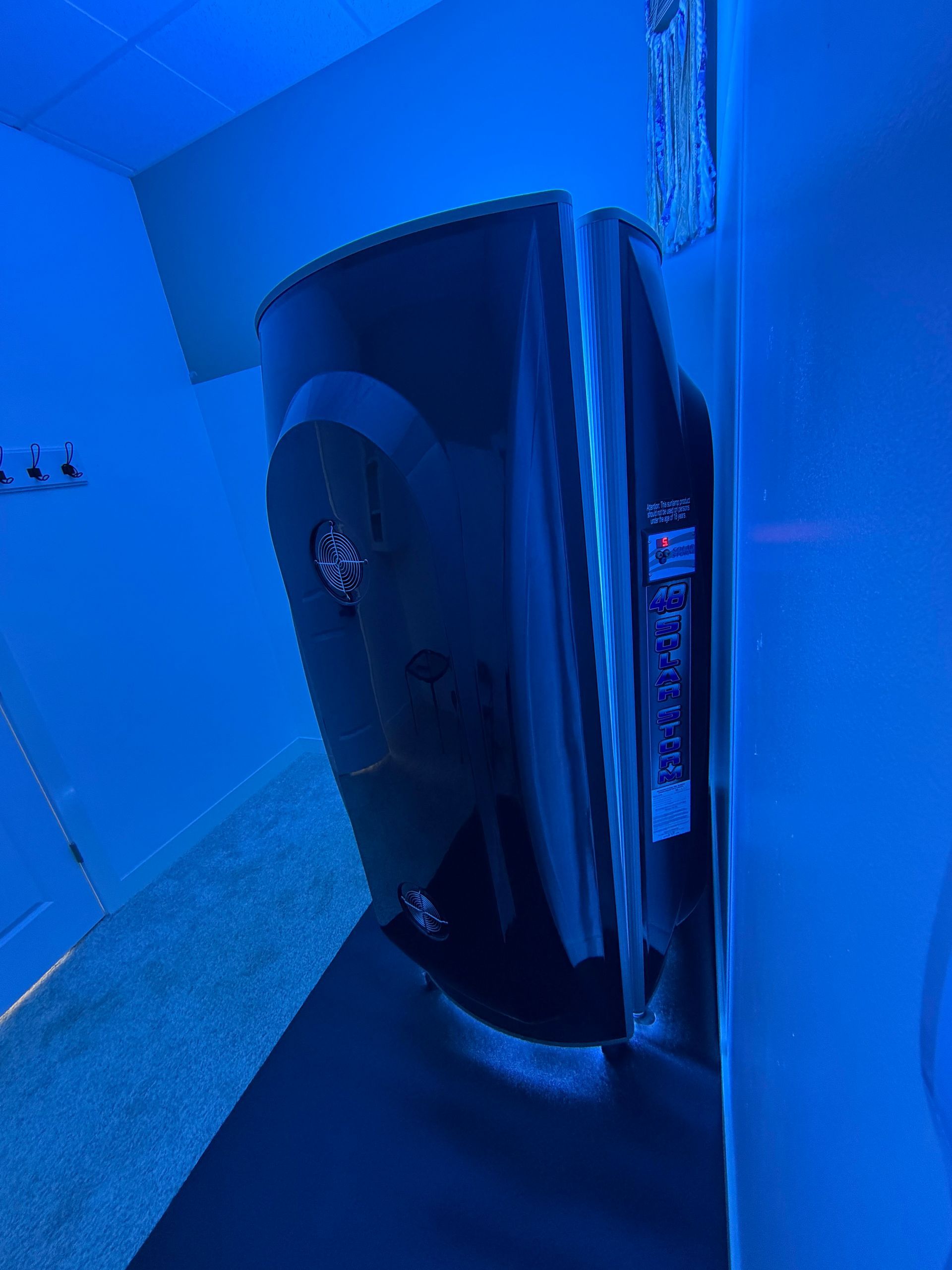 Blue-tinted hallway with a large black wall-mounted fixture or cabinet against a white wall.