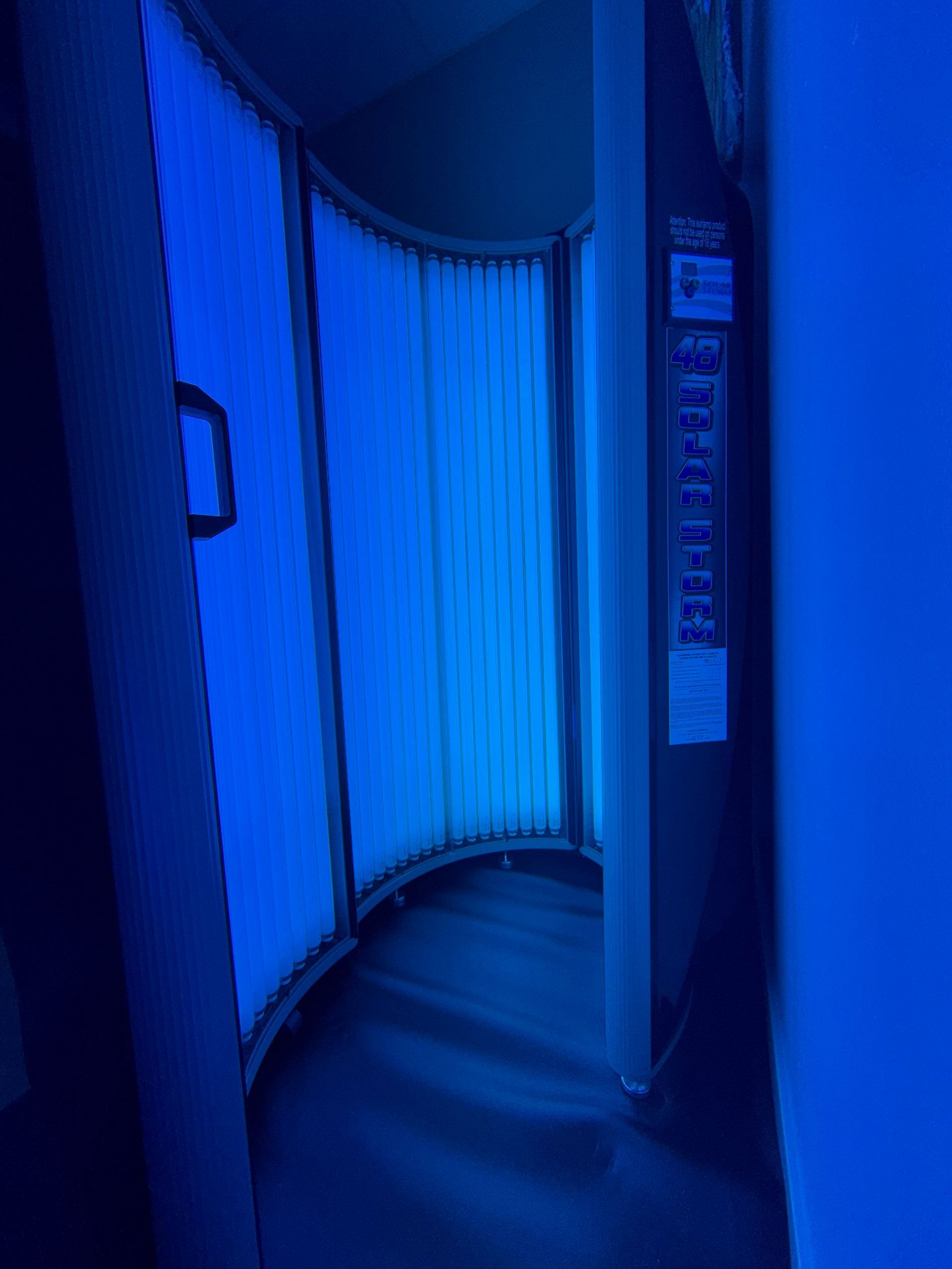Blue-lit tanning booth interior with curved walls and vertical light panels