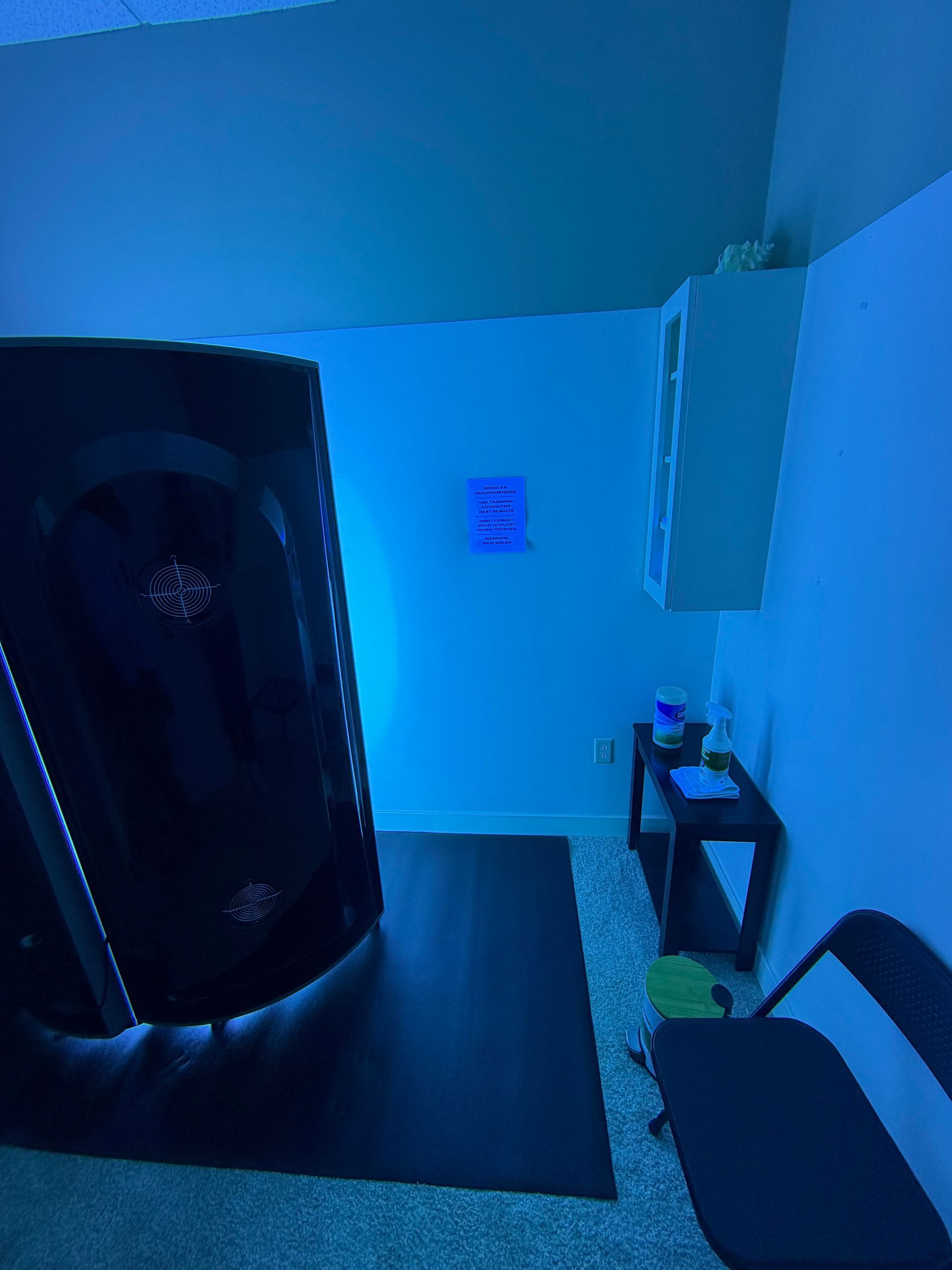 Blue-lit room with a sauna or infrared cabinet, chair, small table, and wall art.