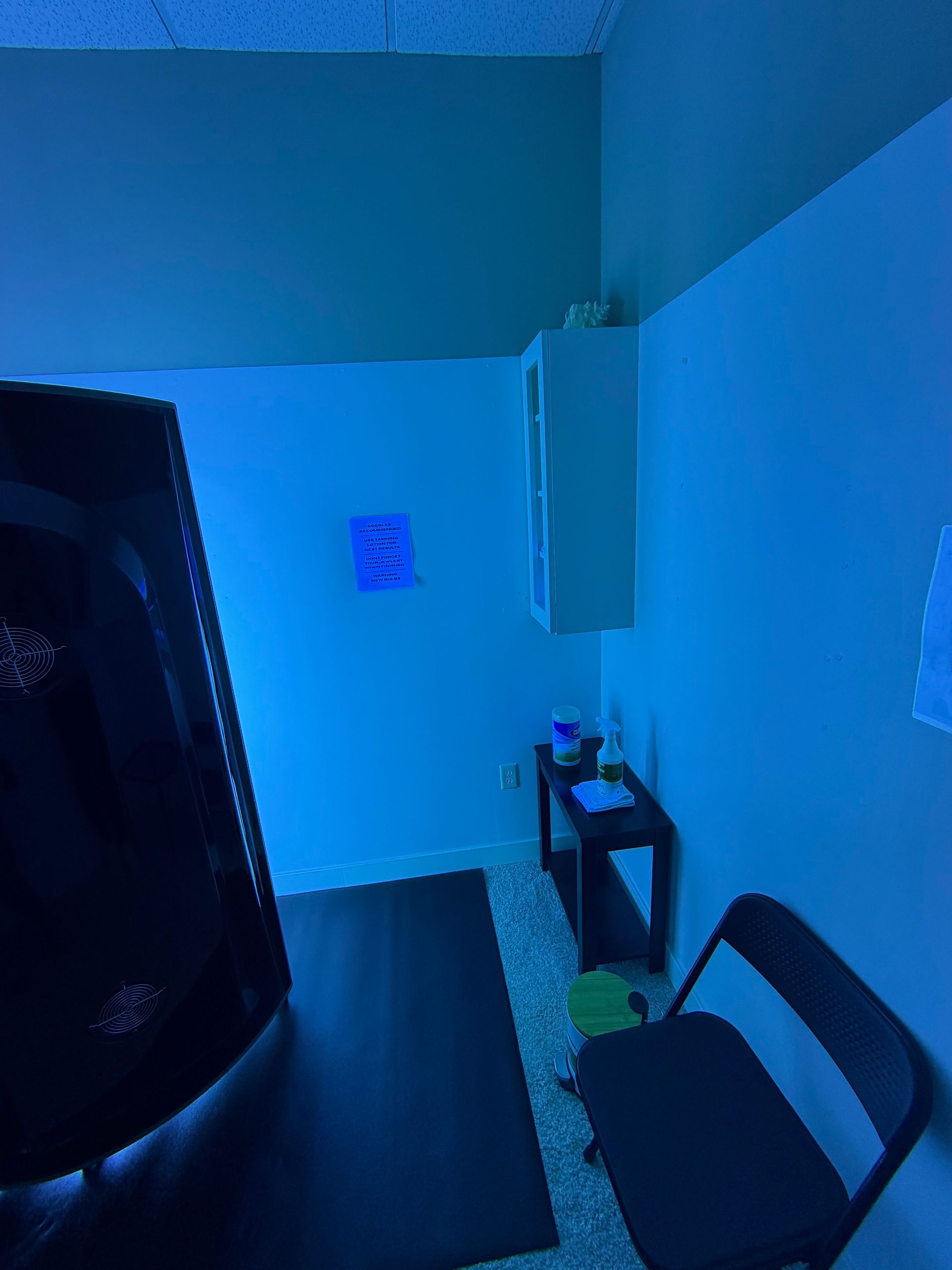 Blue-lit small room with a chair, table, and wall art near the corner.