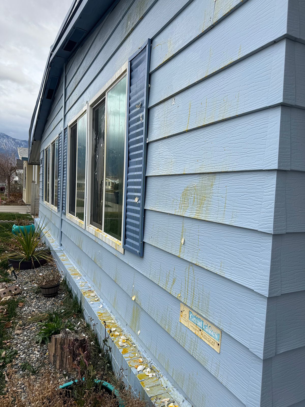 Blue-sided house with a row of windows and blue shutters; visible exterior damage.
