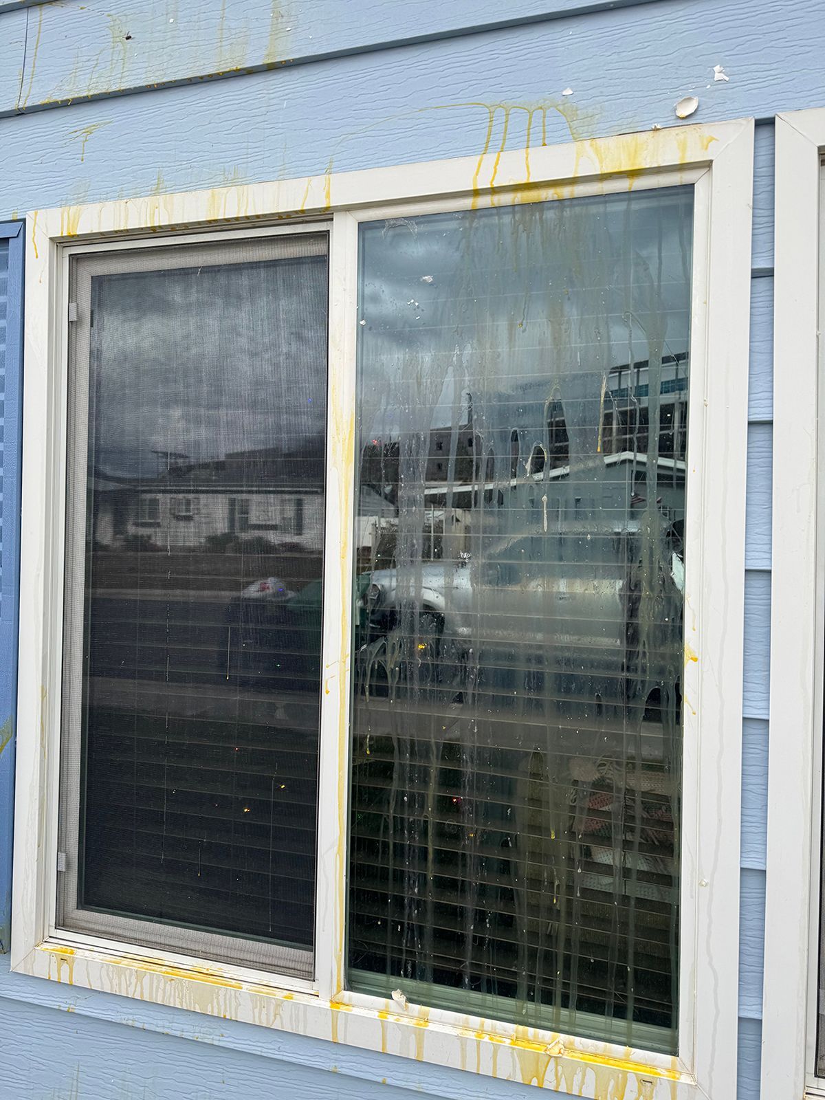 Sliding glass window with dirty glass and yellow streaks, set in a blue siding. The left panel has a screen.