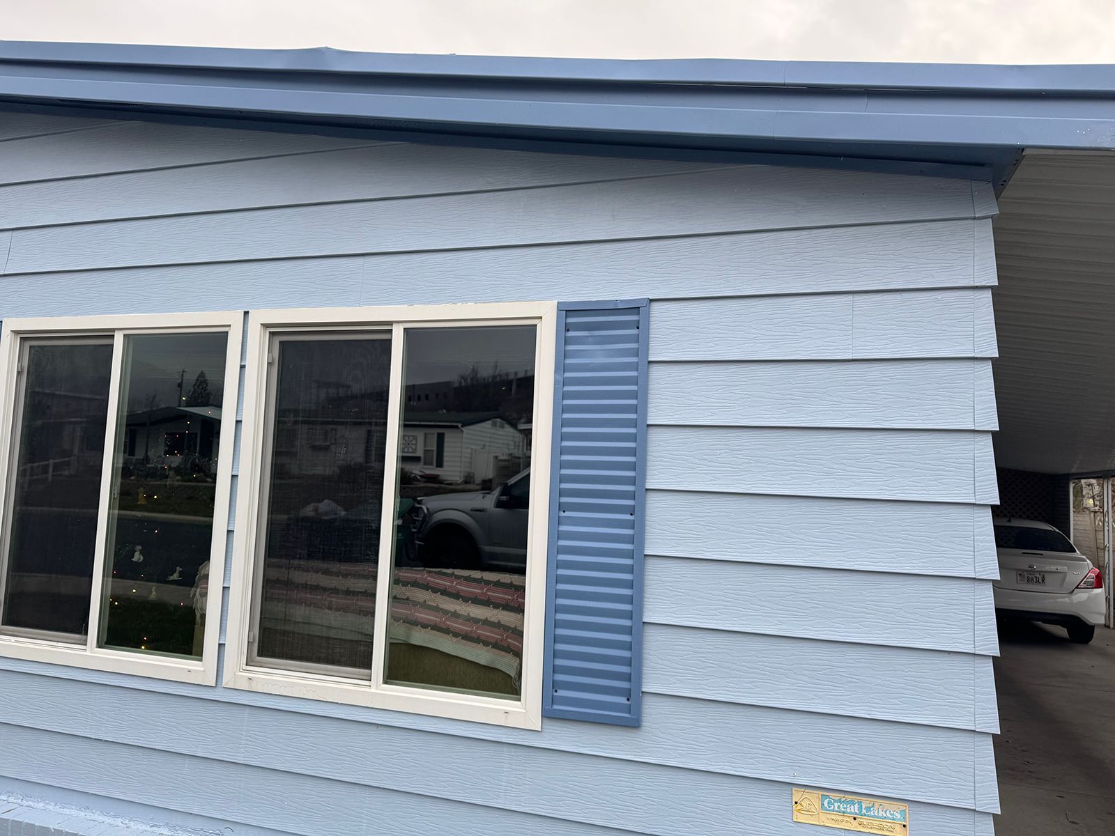 Light blue house with matching siding and shutters, three windows, and carport.