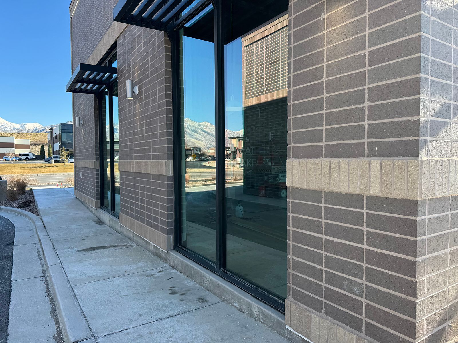 Building with large windows and brick exterior, sidewalk, mountains in the background.