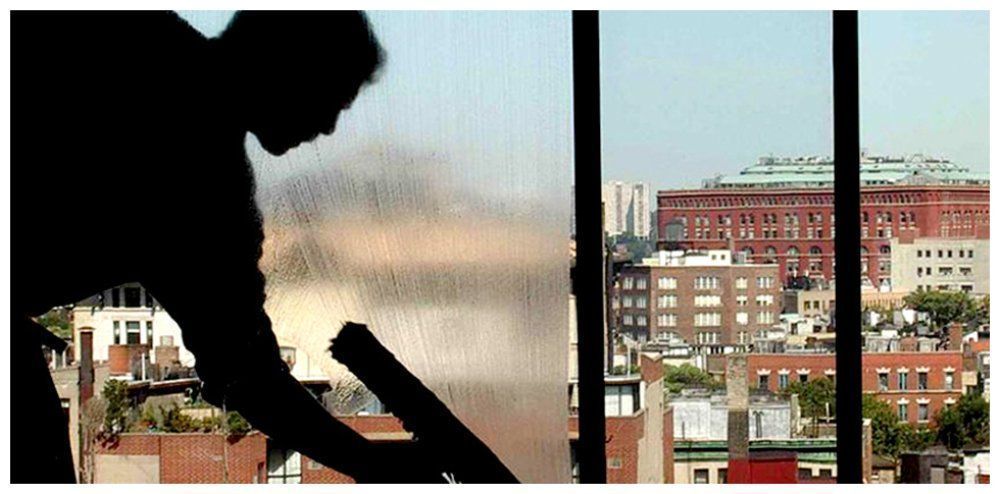 Silhouette of a person cleaning a window, with a city view visible through the window.