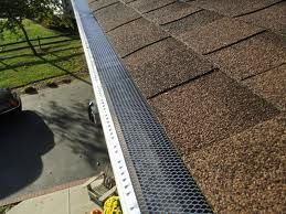 Gutter with mesh guard on a brown shingle roof, angled view.