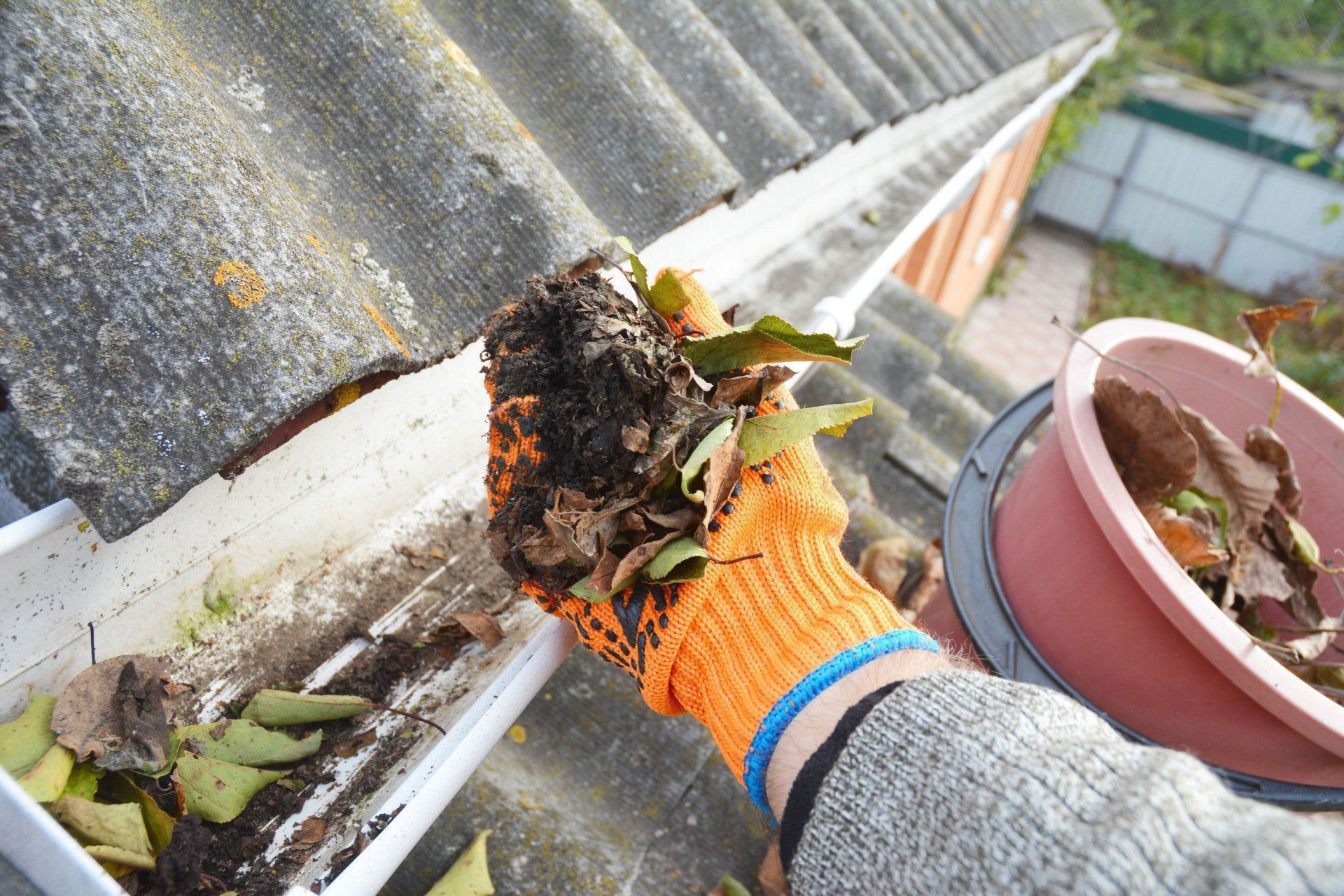 Person wearing orange work gloves cleans debris from a gutter.
