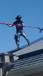 Person on rooftop holding a long tool against a blue sky.