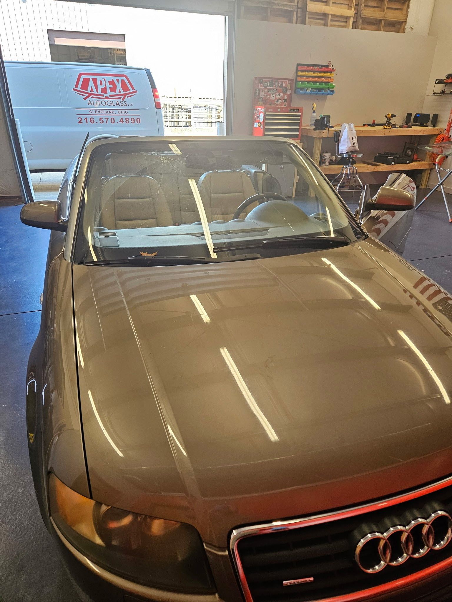 An Audi car is parked in a garage with a white van in the background.
