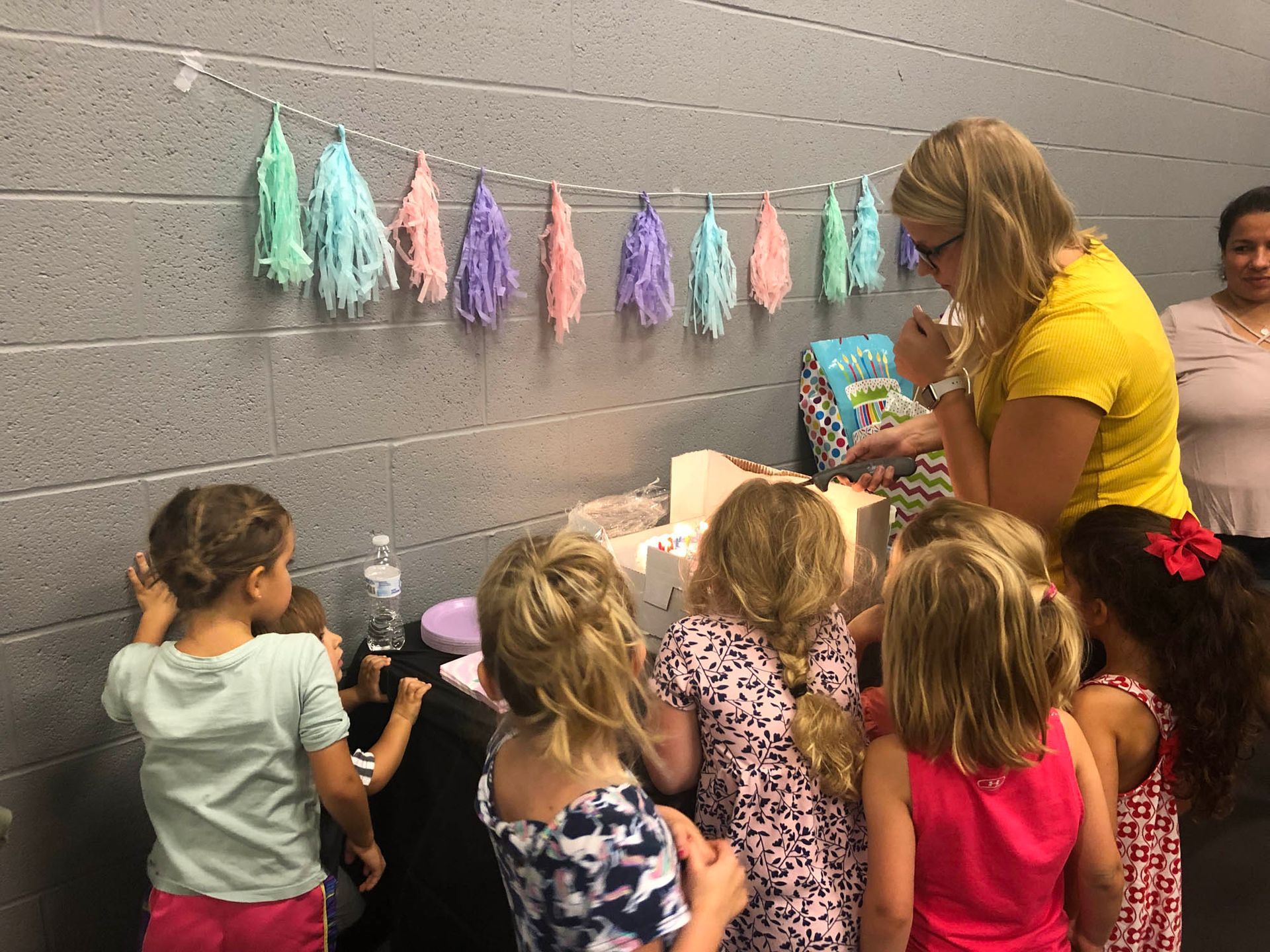 A group of young girls are standing around a table at a birthday party.