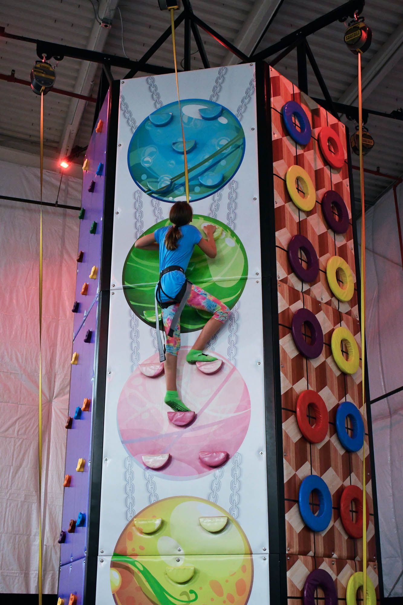 A girl is climbing up a climbing wall with circles on it.