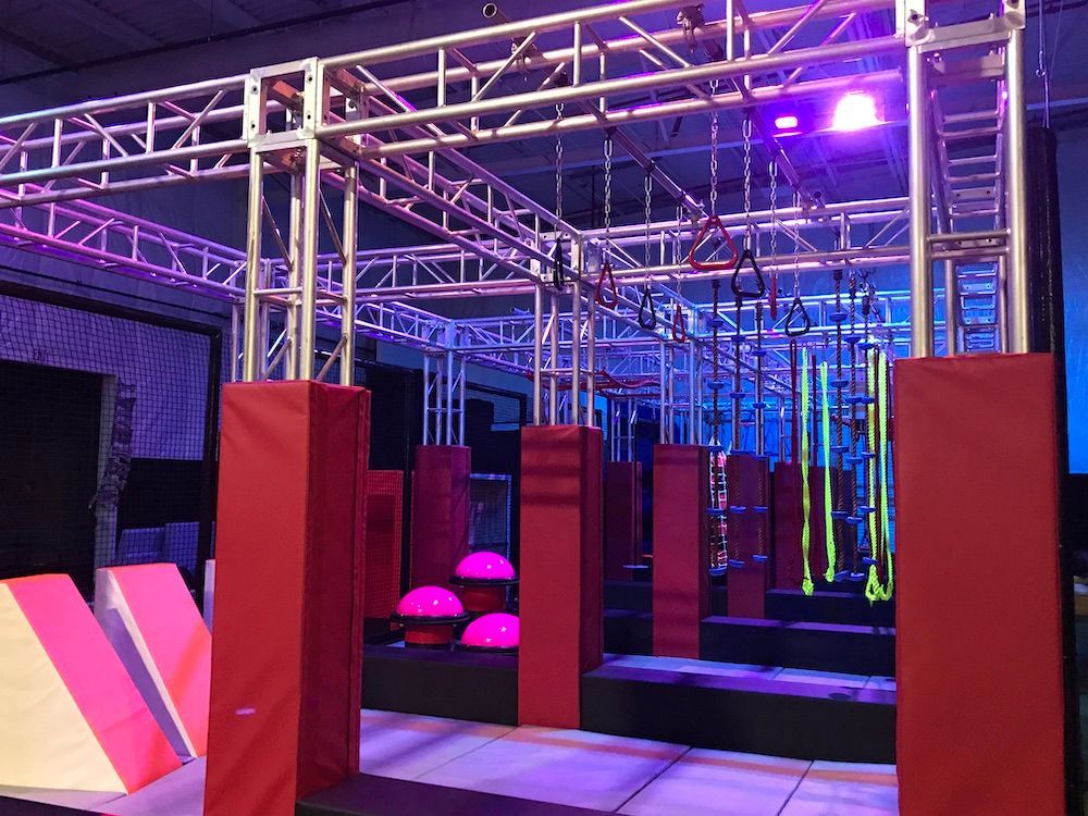A ninja warrior course in a gym with purple lights.