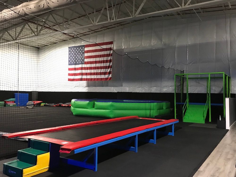 There is a trampoline in the middle of the room with an american flag hanging from the ceiling.