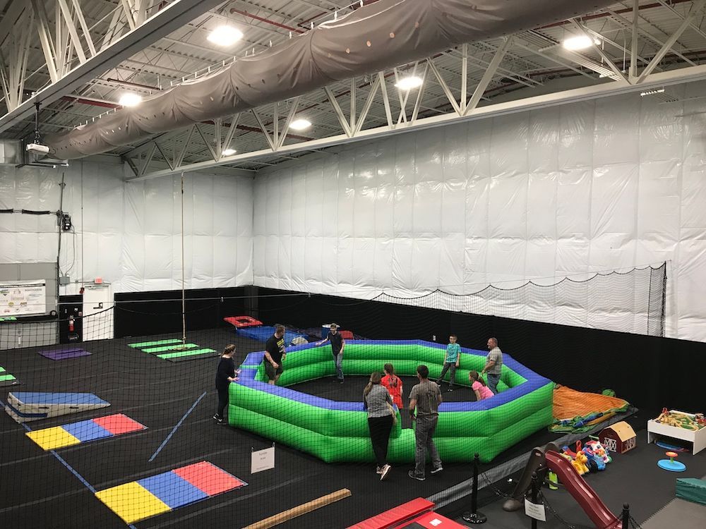 A group of people are standing around a large inflatable circle in a gym.