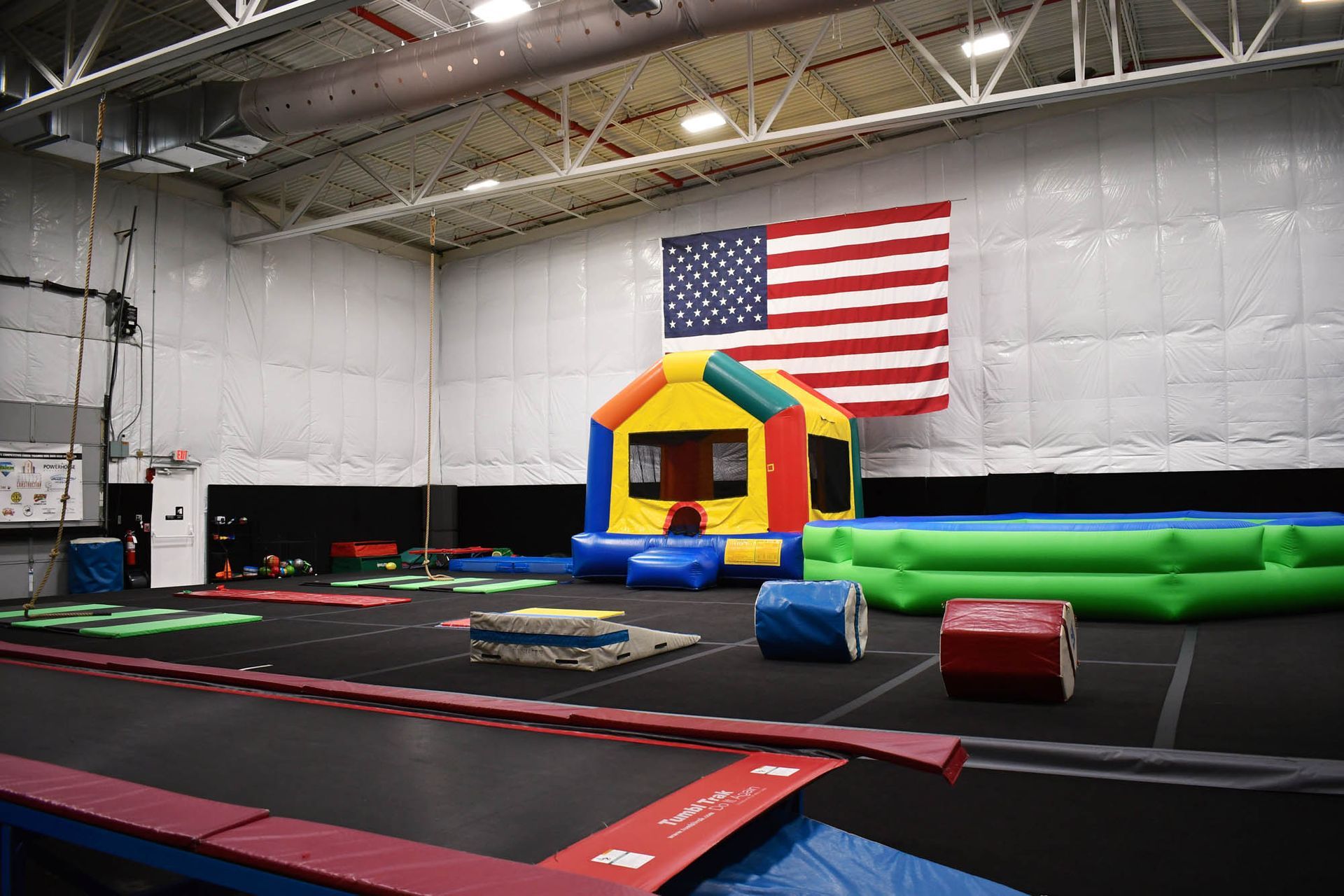 A large indoor gym with a bouncy house and an american flag on the wall.