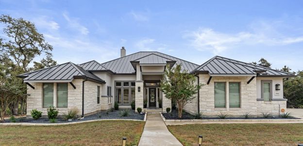 Modern single-story stone house with a metal roof and centered front walkway