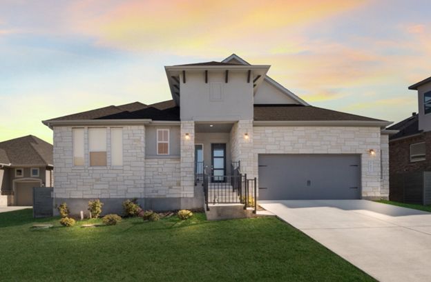 Modern suburban house with gray stone exterior, two-car garage, and front lawn at sunset