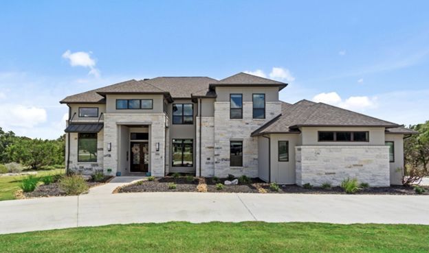 Modern two-story stone house with a three-car garage and wide front lawn under a blue sky
