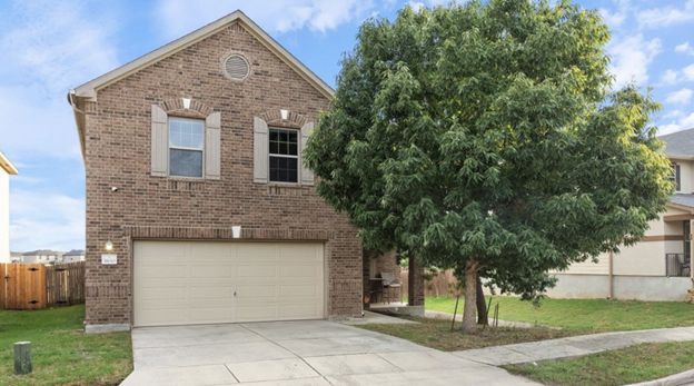 Two-story brick house with beige garage and large tree in front yard