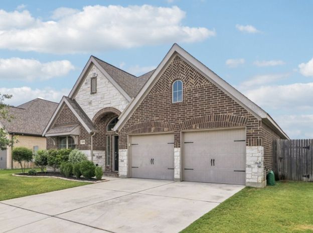 Suburban brick house with two-car garage, driveway, and neatly kept lawn under a blue sky