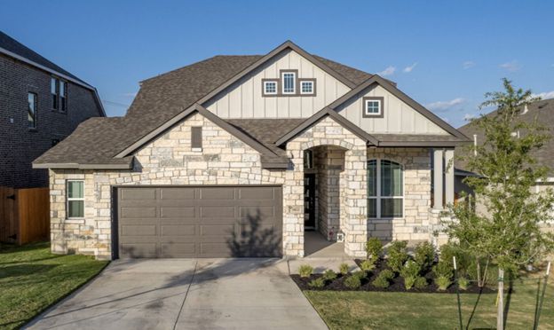 Modern single-story suburban house with stone facade, two-car garage, and a front lawn on a sunny day