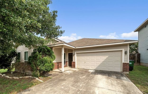 Single-story suburban house with two-car garage, driveway, and front porch under a blue sky