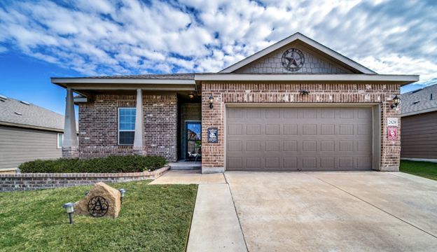 Single-story suburban brick house with a two-car garage and a concrete driveway under a cloudy sky