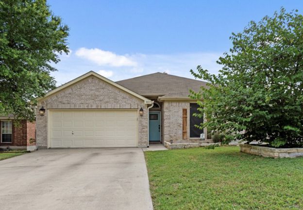 Suburban brick house with two-car garage, driveway, and green lawn under a blue sky